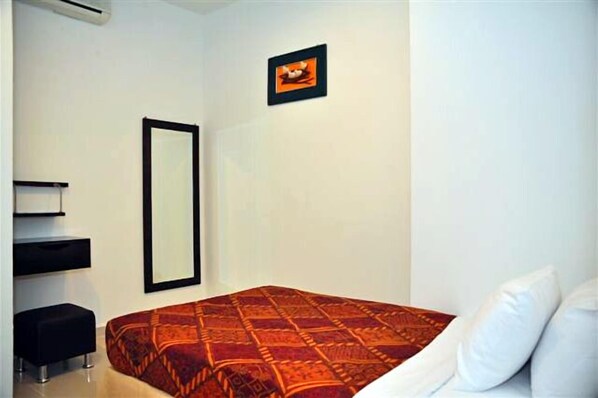 A bedroom with a bed, a large mirror, a small stool, and a framed picture on the wall.