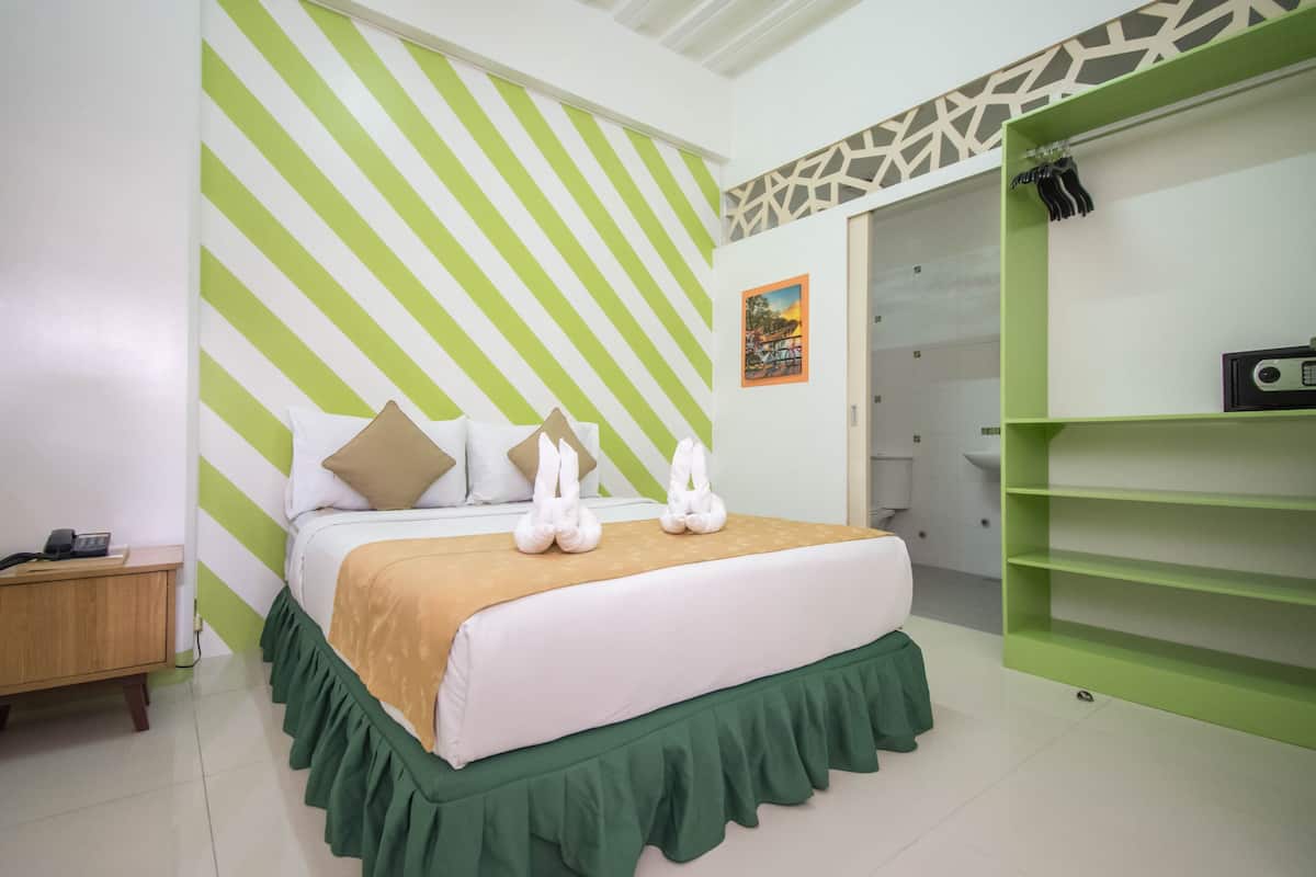 Ein ordentlich eingerichtetes Schlafzimmer mit einem Bett, einer Wand mit grün-weißen Streifen, einem kleinen Nachttisch und einem grünen Regal.