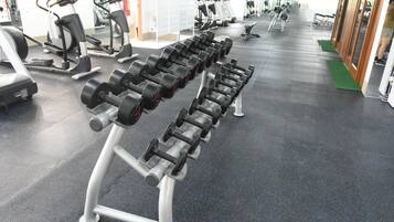 A gym with rows of dumbbells on a rack, exercise machines, and a mirrored wall.