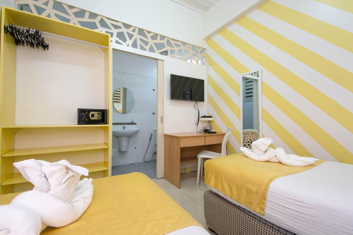 Ein Hotelzimmer mit zwei Betten, einem Schreibtisch, einem Stuhl, einem Fernseher, einem Kleiderschrank und einem Badezimmer.