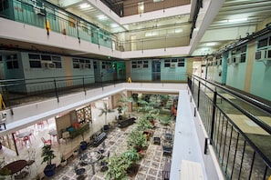 A multi-level atrium with a central courtyard featuring potted plants and outdoor seating. - Alicia Tower Residences - Adult Only - Hostel (Cebu City)