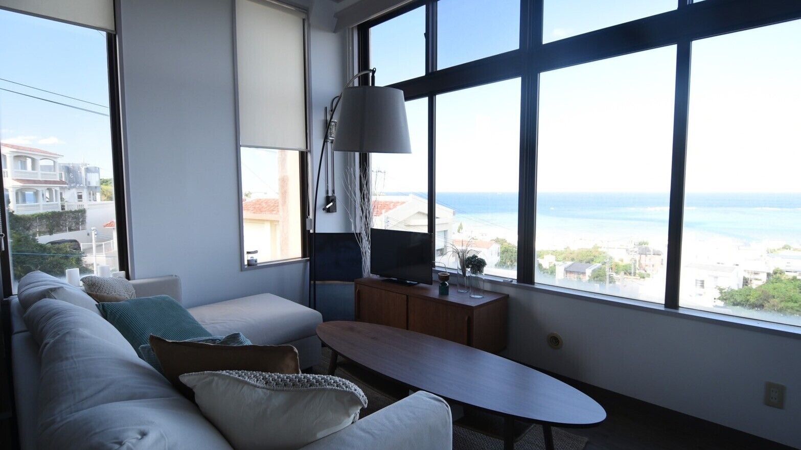 Ein modernes Wohnzimmer mit einer Couch, einem kleinen Tisch, einem Fernseher und großen Fenstern mit Blick auf das Meer.