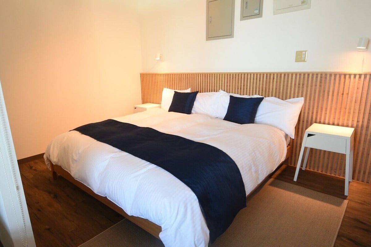 A hotel room with a bed, a bedside table, a nightstand, and a wall-mounted light fixture.