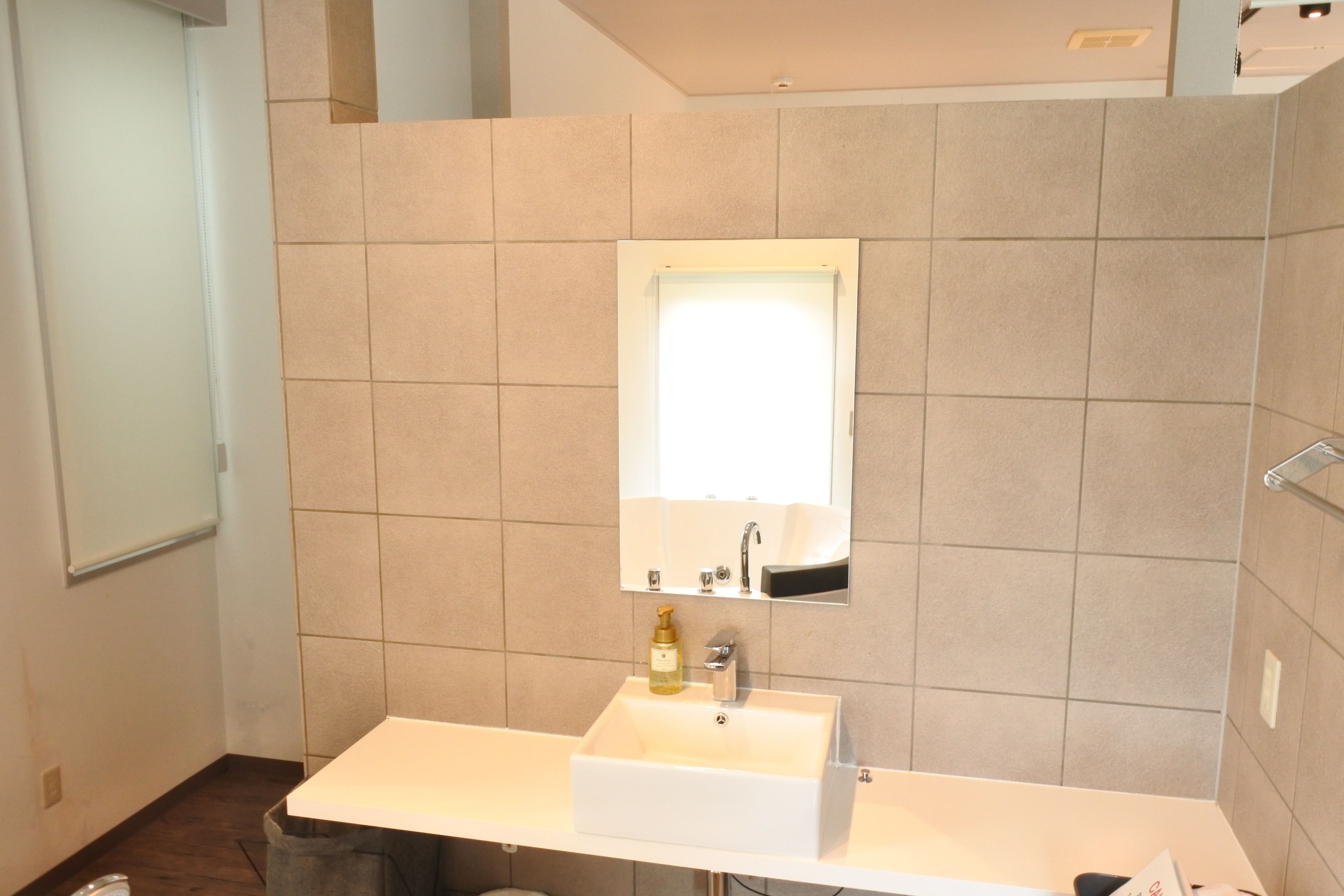 A bathroom with a white sink, a mirror, and beige tiles.