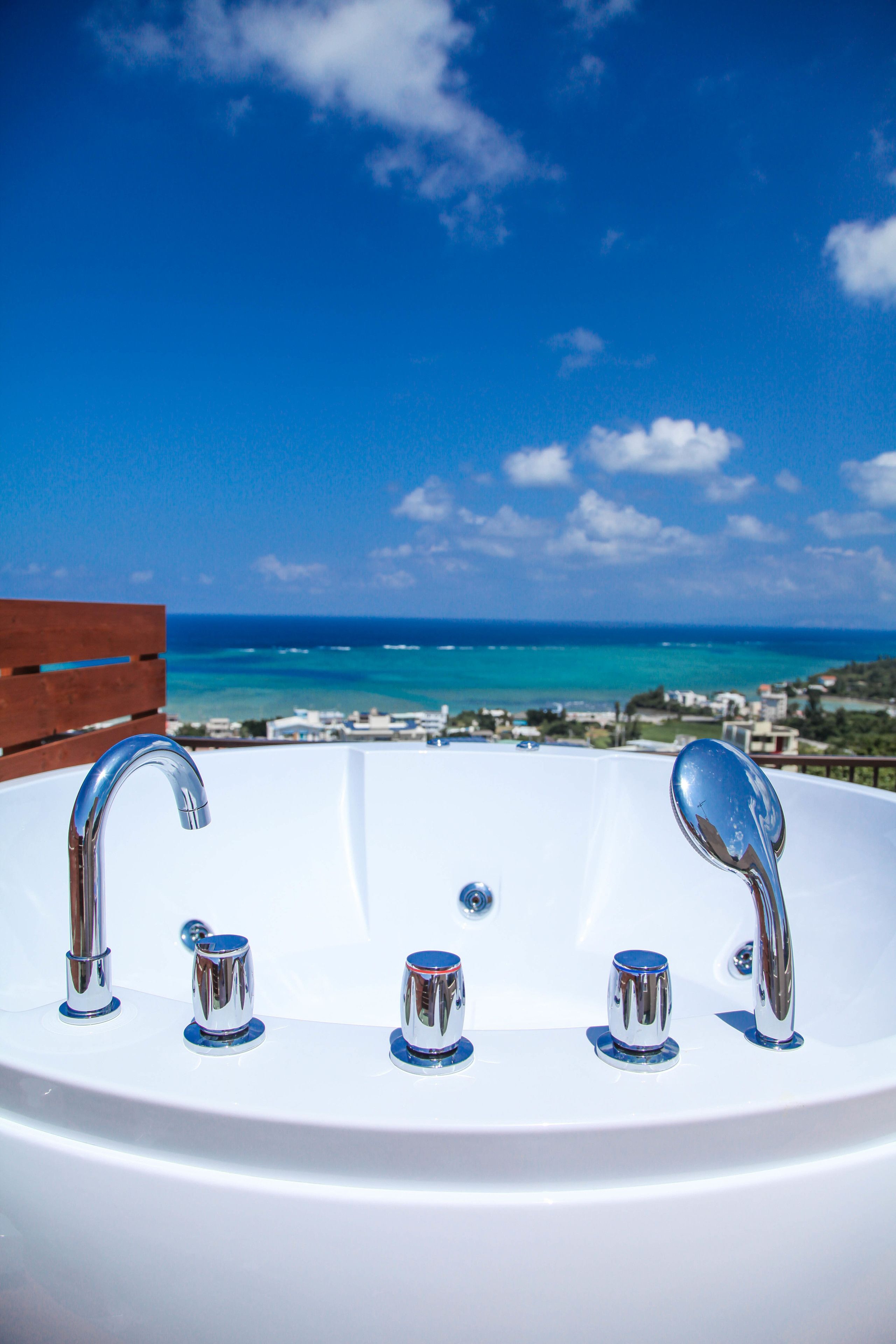 A white bathtub with two faucets, set against a backdrop of a clear blue sky and a coastal view.