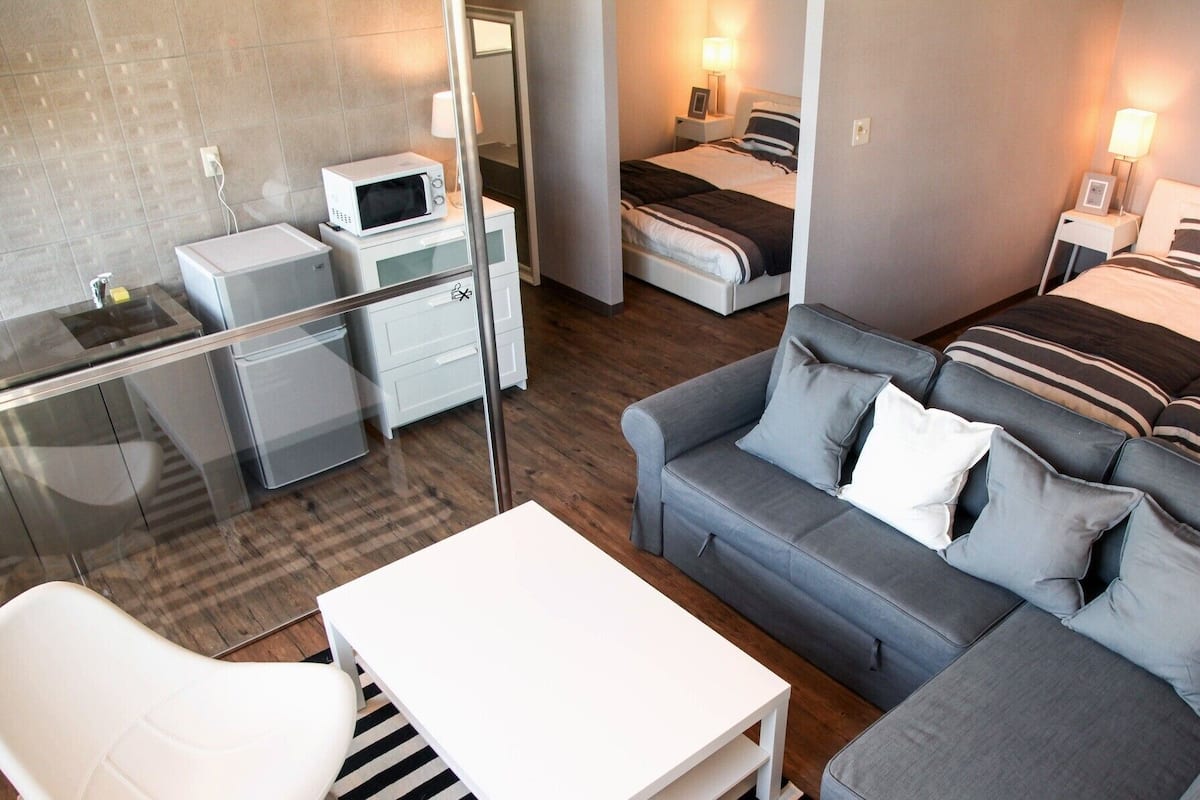 A modern hotel room with a glass partition separating the living area from the kitchenette.