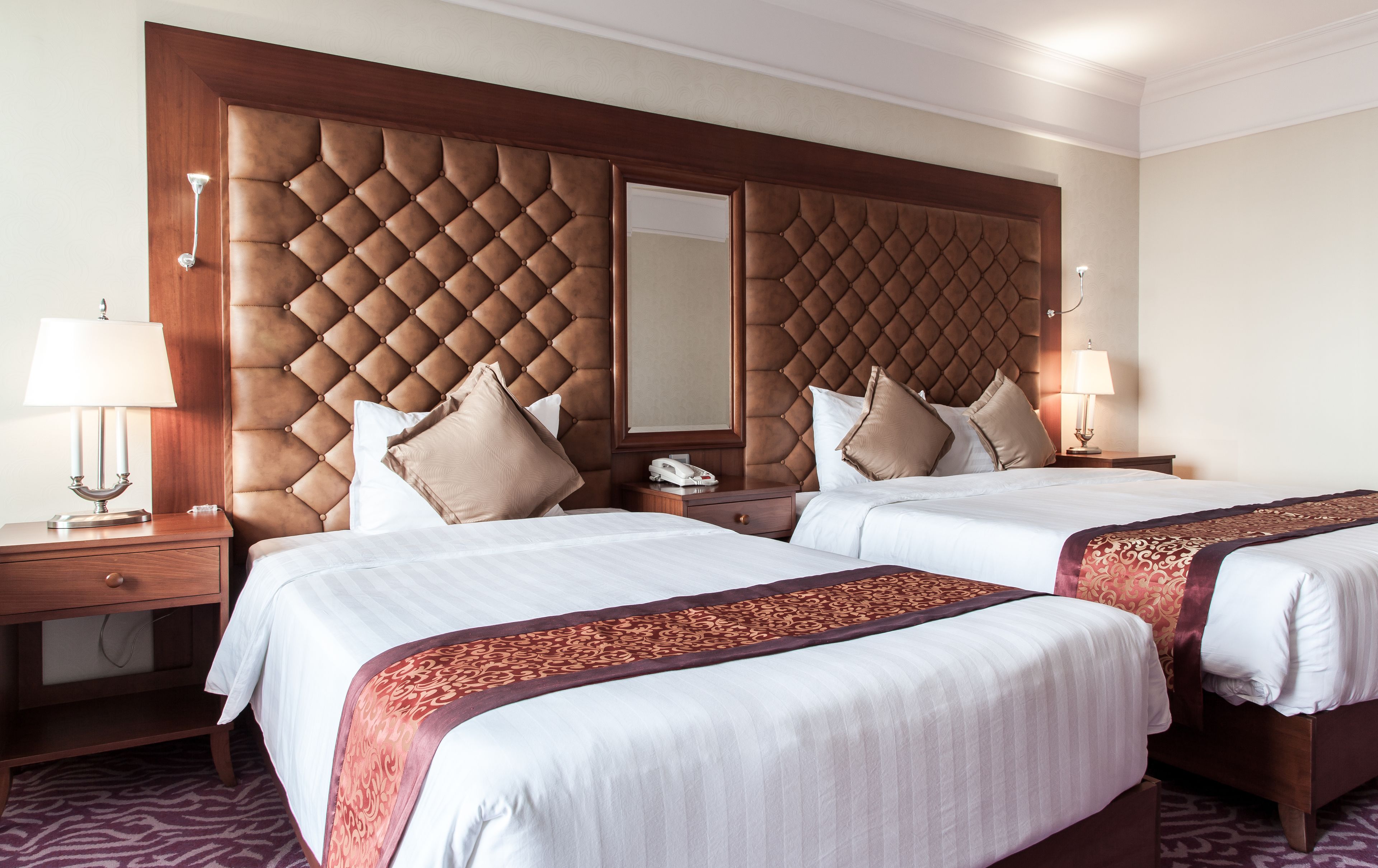 Une chambre d’hôtel avec deux lits, une tête de lit en bois, une table de chevet avec une lampe et une petite table de nuit avec un téléphone.