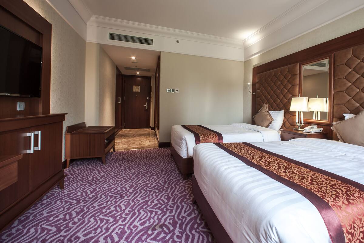 A hotel room with two beds, a large mirror, a television, and a desk.