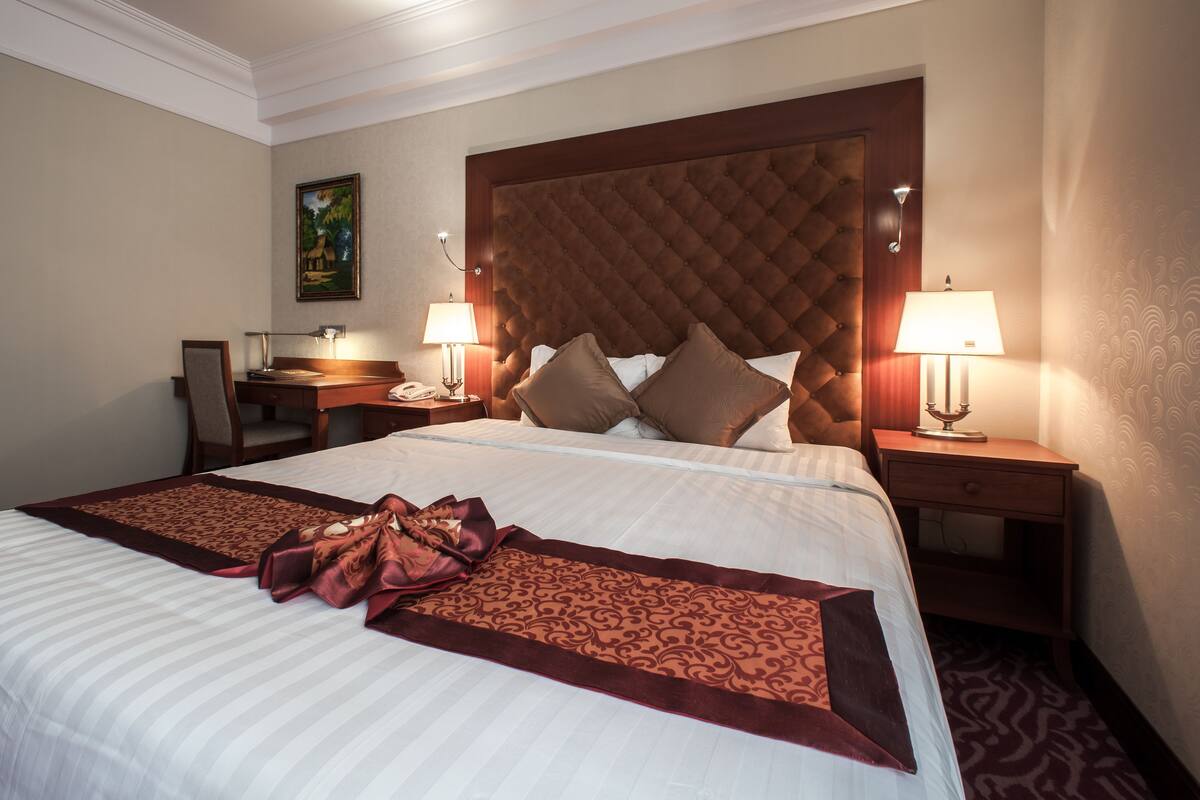 A hotel room with a large bed, two bedside tables with lamps, a desk, and a chair.