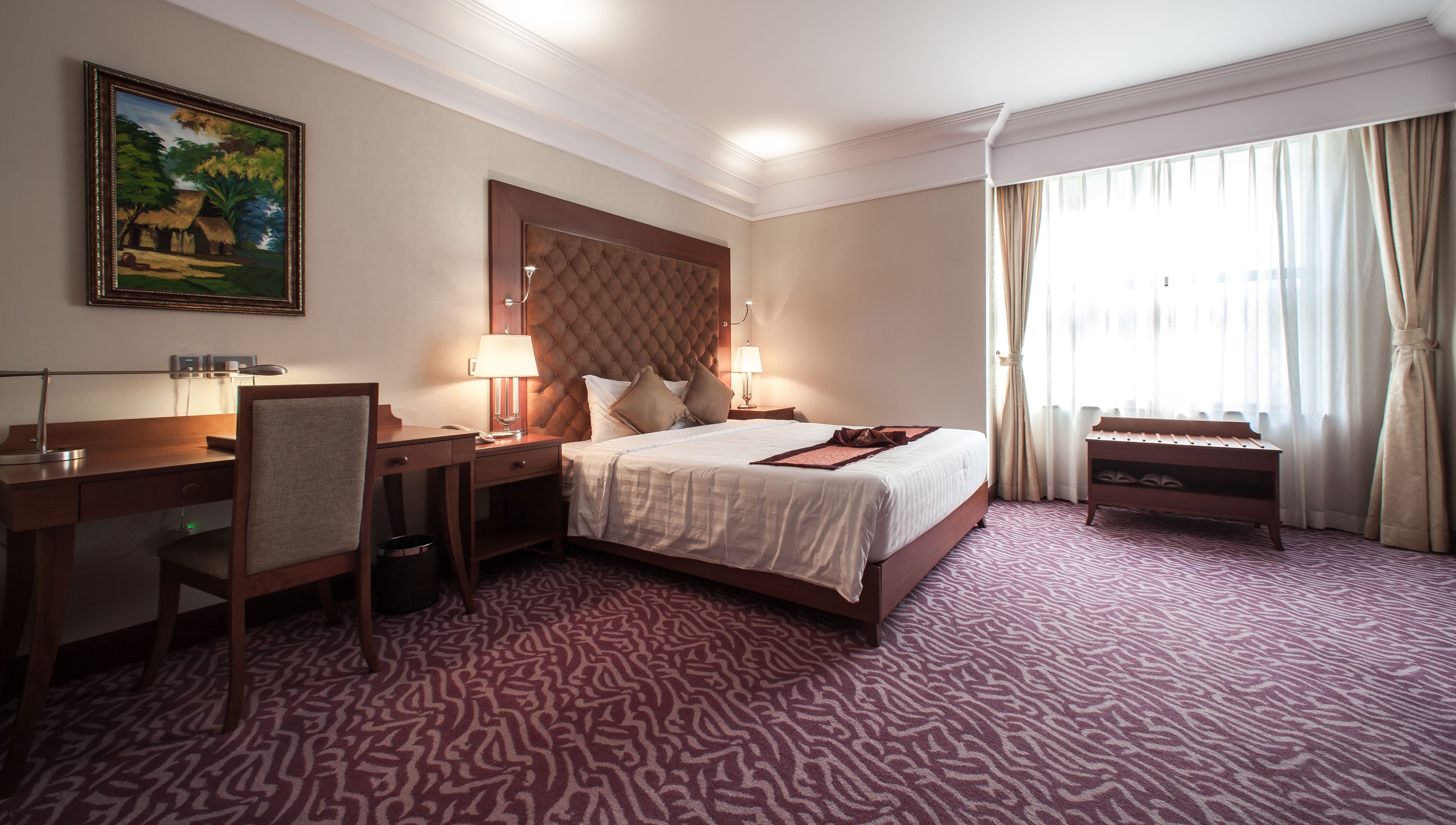 Ein Hotelzimmer mit Bett, Schreibtisch, Stuhl und einem Bild an der Wand.