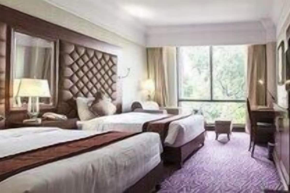 A hotel room with two beds, a large window, and a mirror.