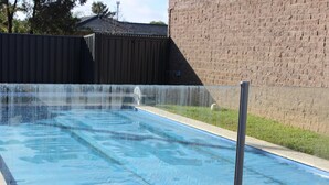 A rectangular swimming pool with a clear blue surface, surrounded by a concrete deck and a brick wall. - Thomas Lodge Motel (Tocumwal)