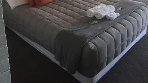 A hotel room with a bed, a sofa, a headboard, and a window with curtains. - Thomas Lodge Motel (Tocumwal)