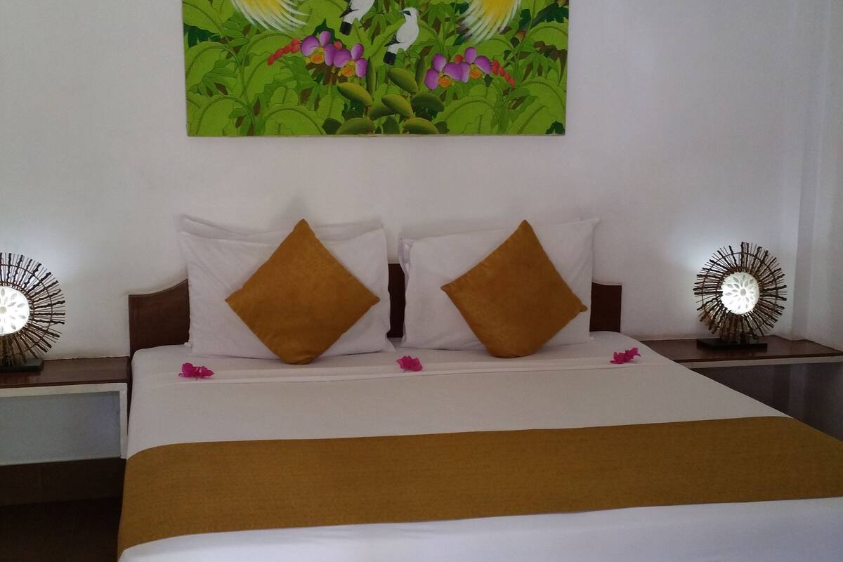 A hotel room with a large bed, white bedding, and a painting of birds on the wall.