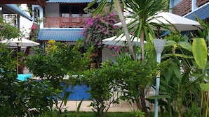 A courtyard with a pool, palm trees, and a building with a blue roof. - Marygio Resort (Gili Trawangan)