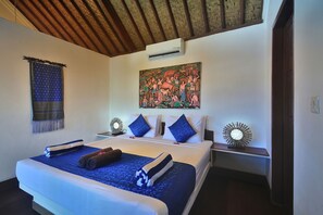 A hotel room with a large bed, two bedside tables, a wall-mounted air conditioner, a decorative painting, and a woven tapestry. - Marygio Resort (Gili Trawangan)