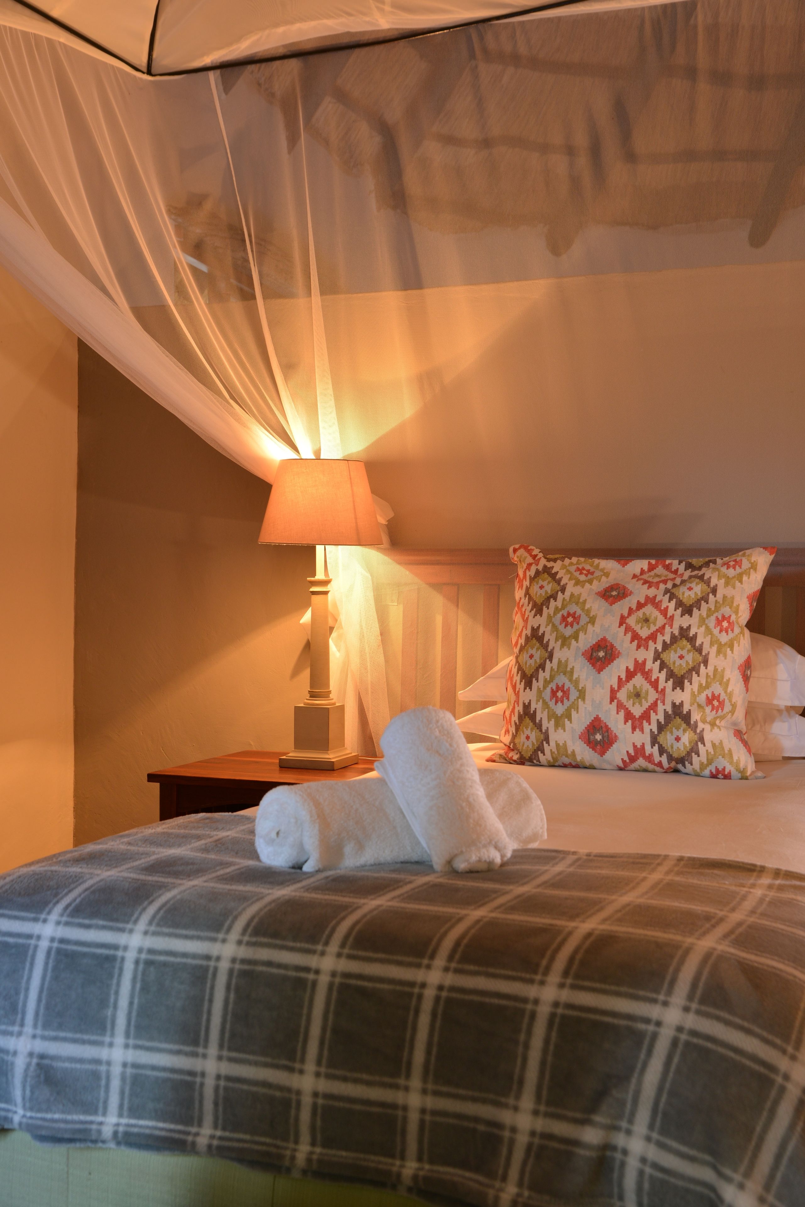 Una cama bien hecha con colcha escocesa, un cojín decorativo y una lámpara de noche.