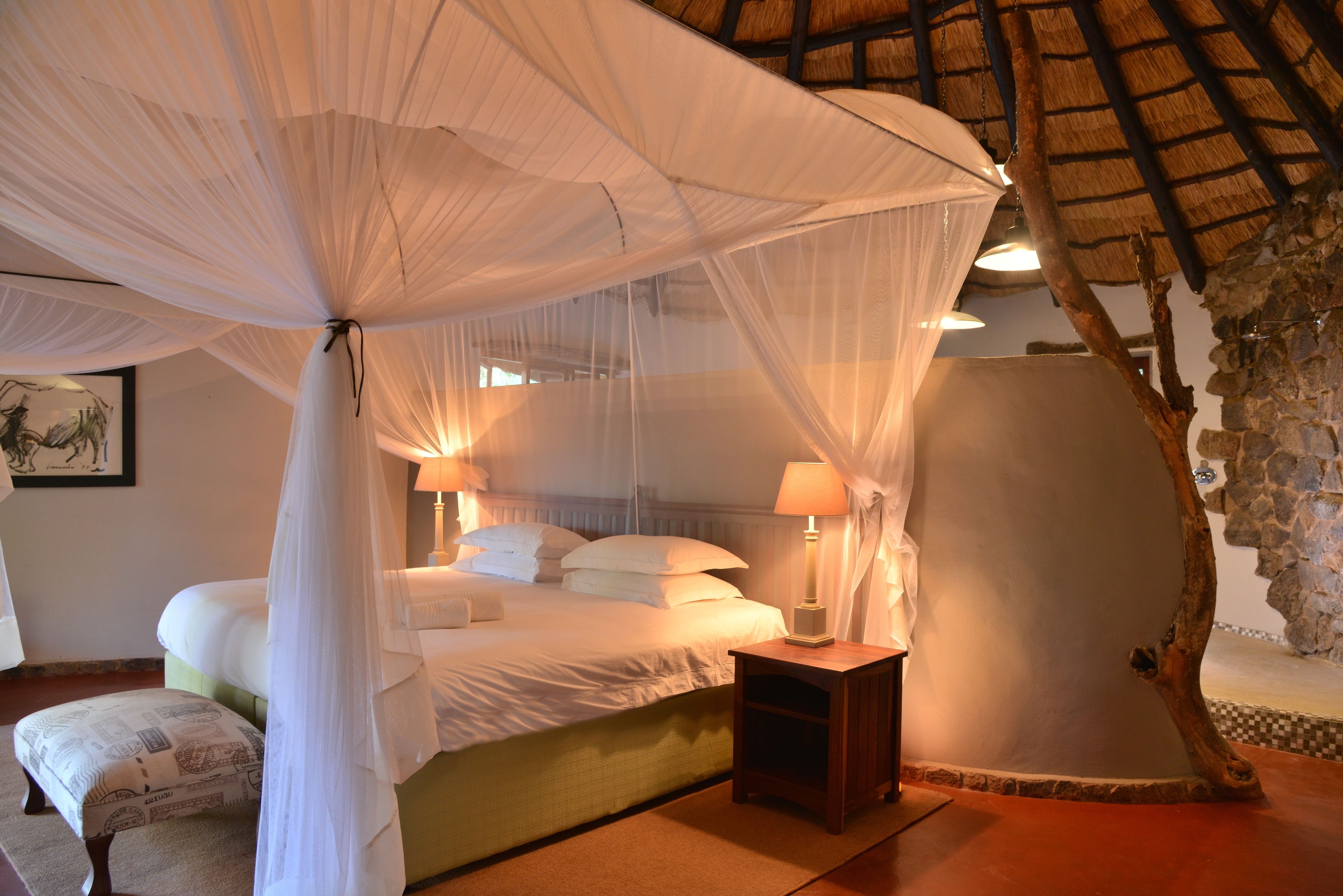 A bedroom with a canopy bed, bedside lamps, and a stone wall.