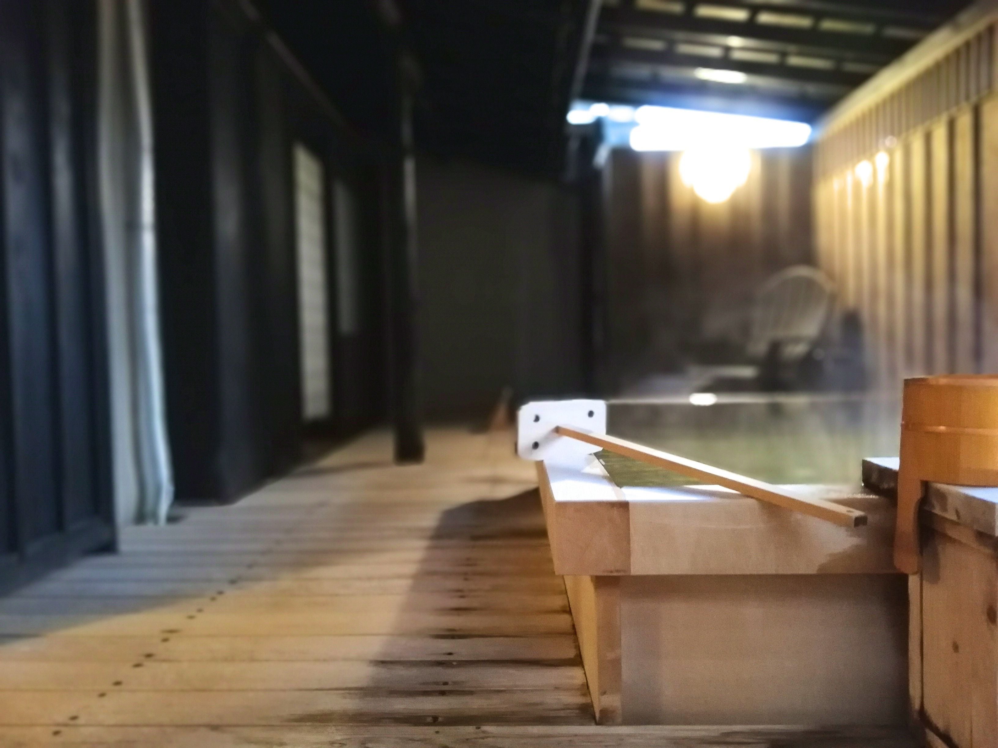 A wooden bench with a slatted design, positioned in a dimly lit corridor with a high ceiling and metal beams.