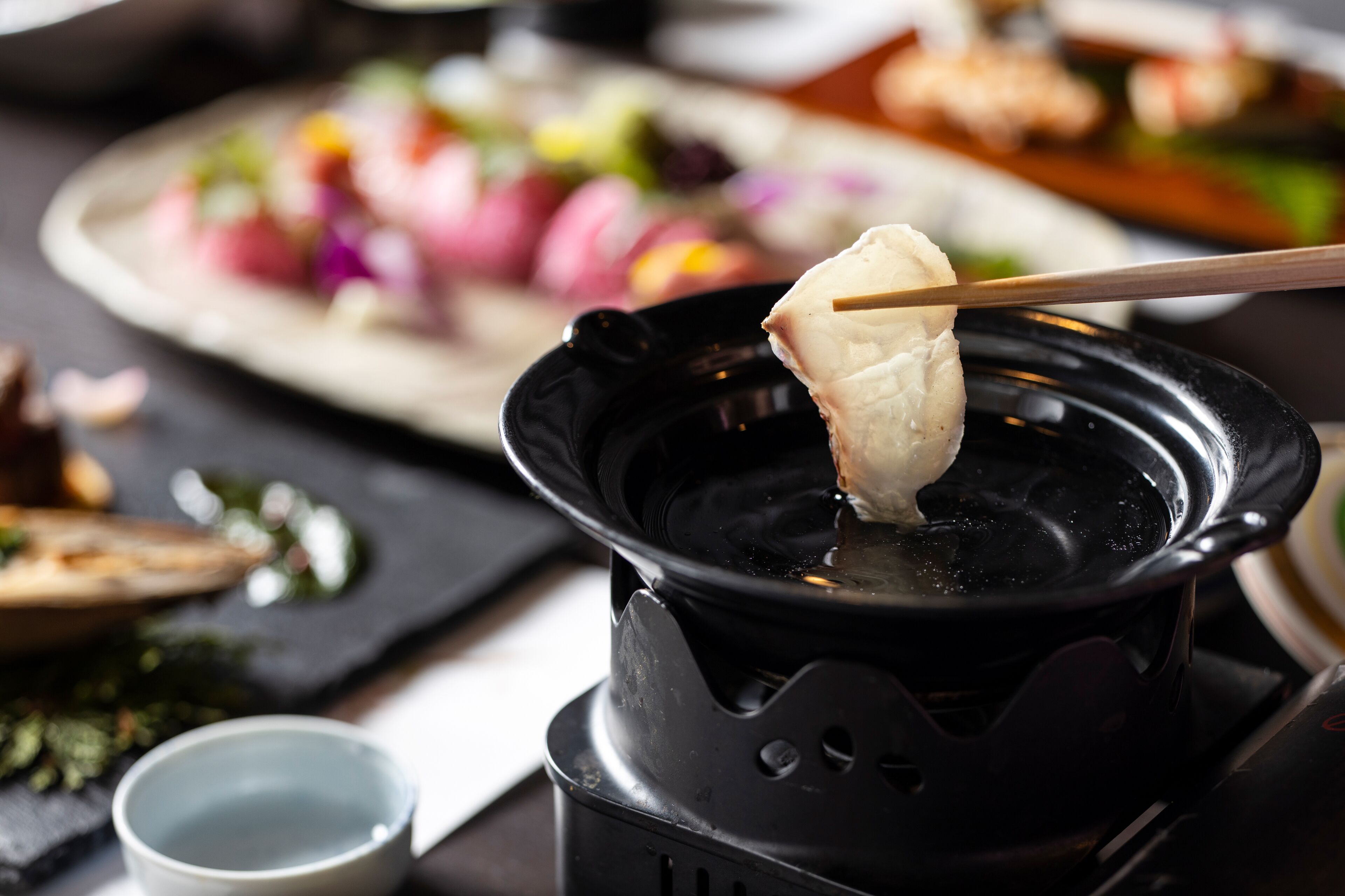 A hot pot setup with a variety of food items in the background.