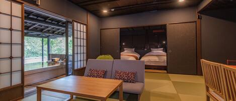 A traditional Japanese-style room with tatami flooring, a low wooden table, a sofa with cushions, and sliding doors leading to a sleeping area.