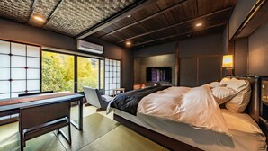 Un dormitorio moderno con una cama grande, un escritorio y vistas a árboles a través de amplios ventanales.