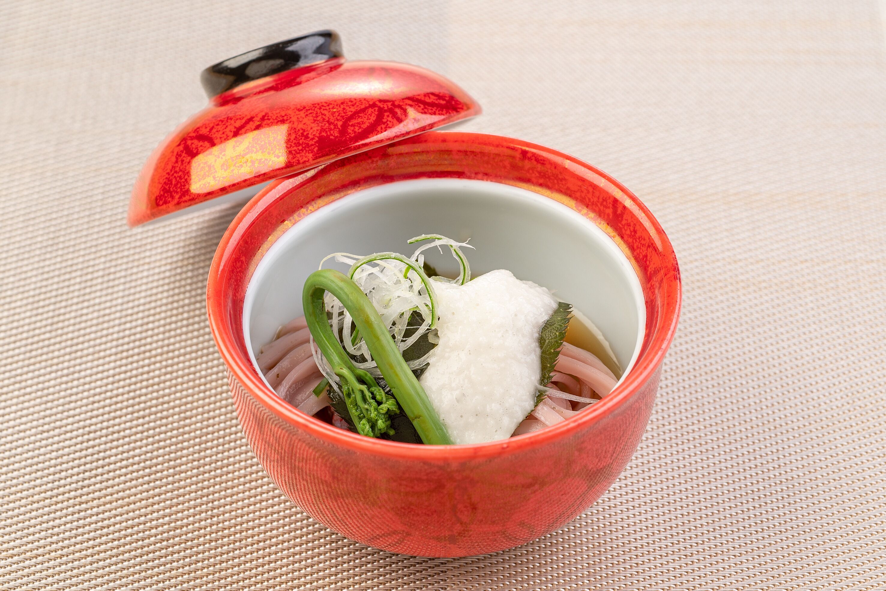 A bowl of food with a red lid on a woven mat.