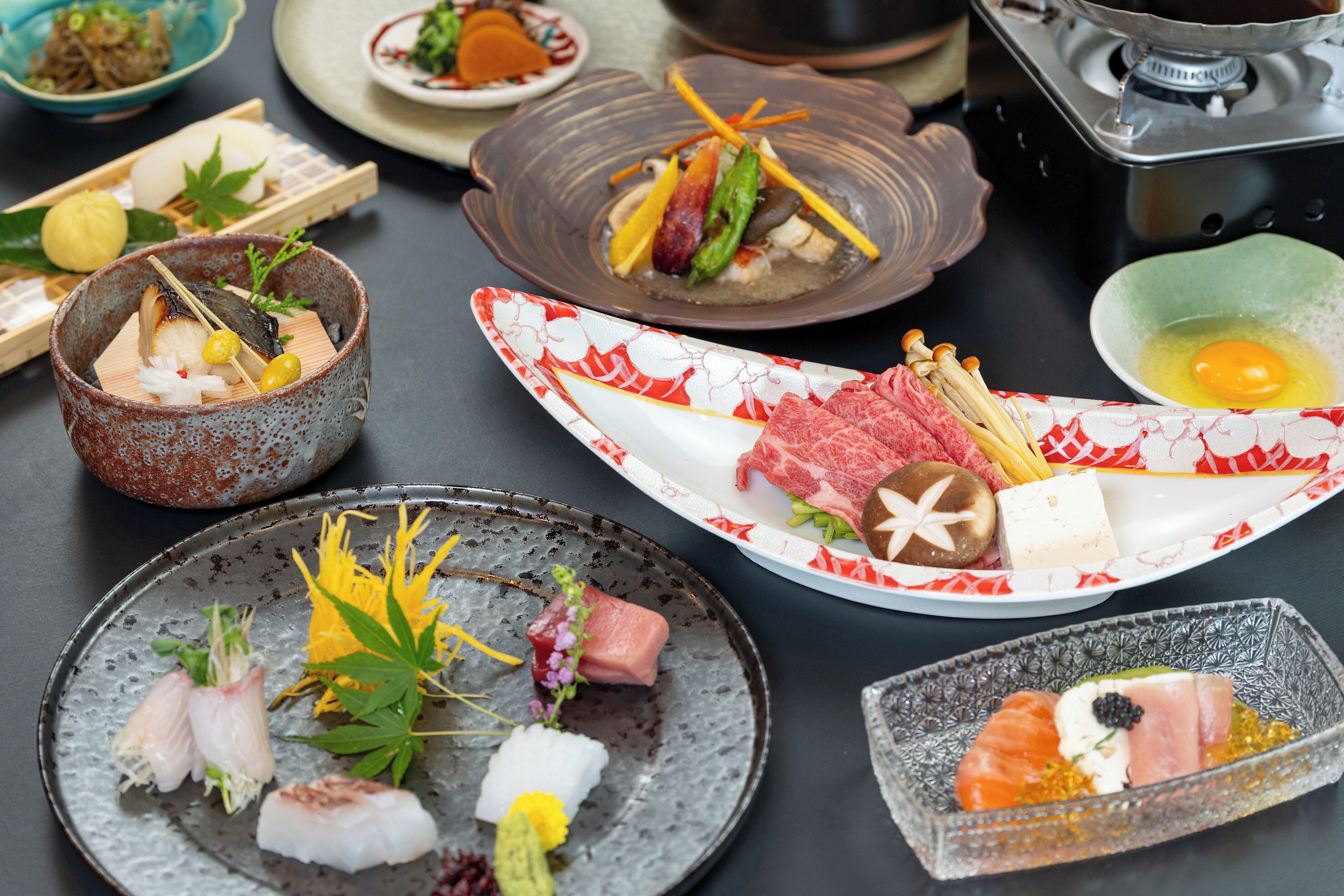 Une variété de plats japonais sont disposés sur une table, notamment des sushis et des sashimis, avec des baguettes et une théière visibles.