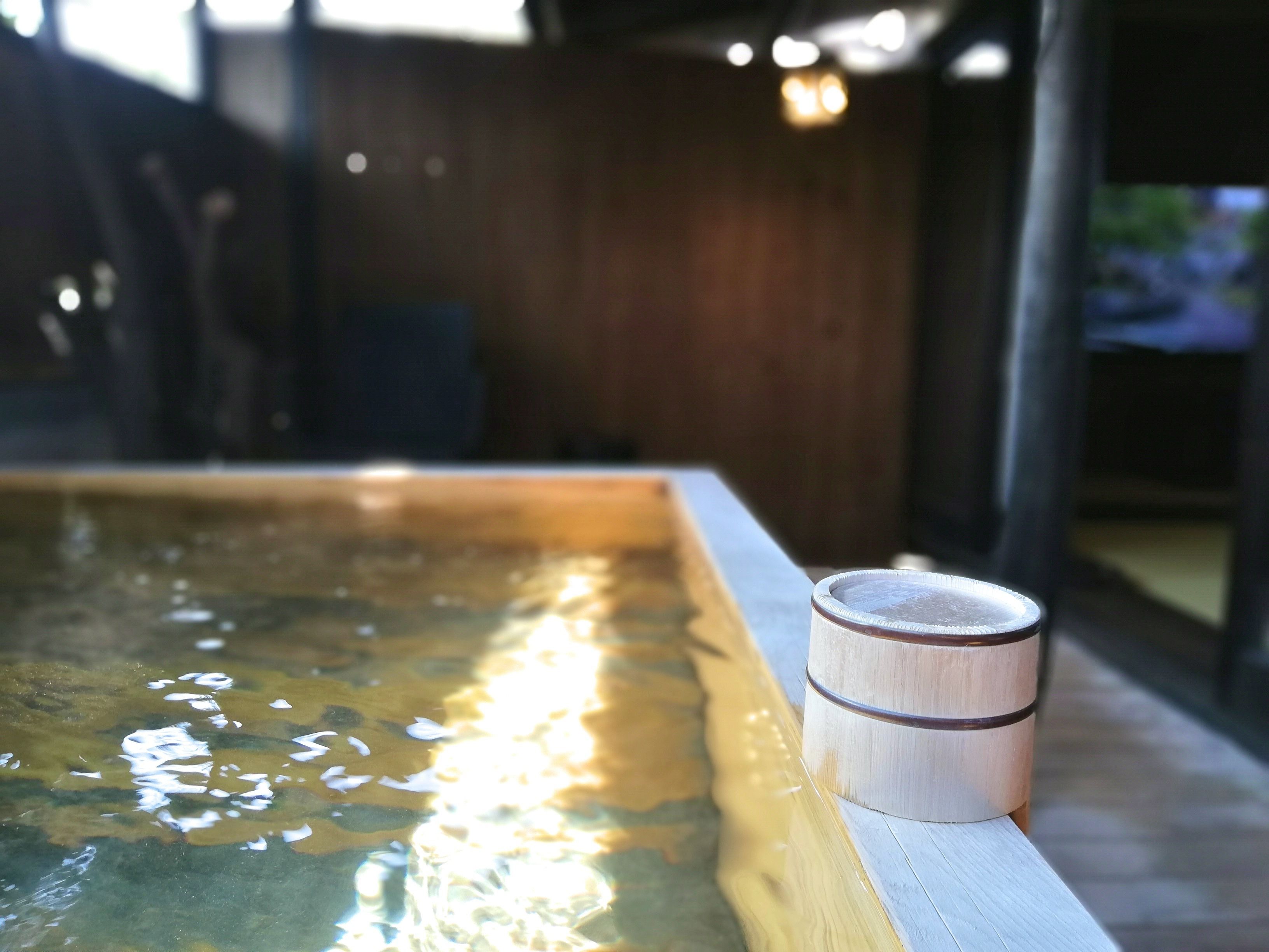 A wooden table with a cup on it, next to a pool with water reflecting sunlight.