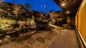 Un jardín japonés tradicional con un estanque de carpas koi, linternas de piedra y un edificio de madera con tejado inclinado.