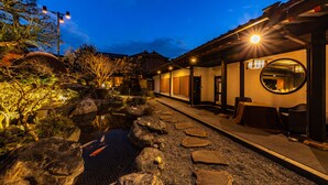 Un edificio de estilo japonés tradicional con un estanque de carpas koi, un sendero de piedra y una zona de estar al aire libre.
