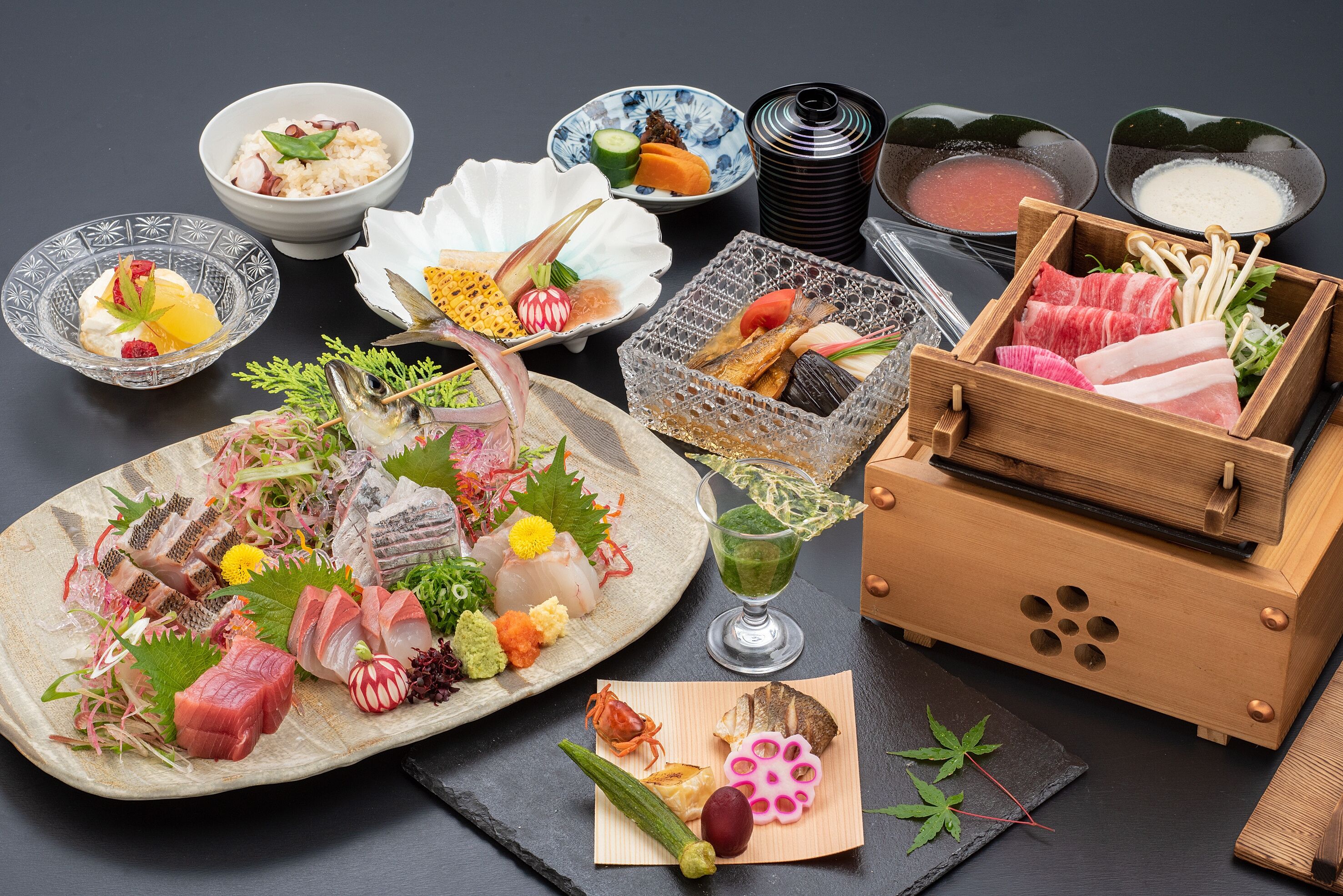 A variety of Japanese dishes including sashimi, rice, and soup, arranged on a dark table.