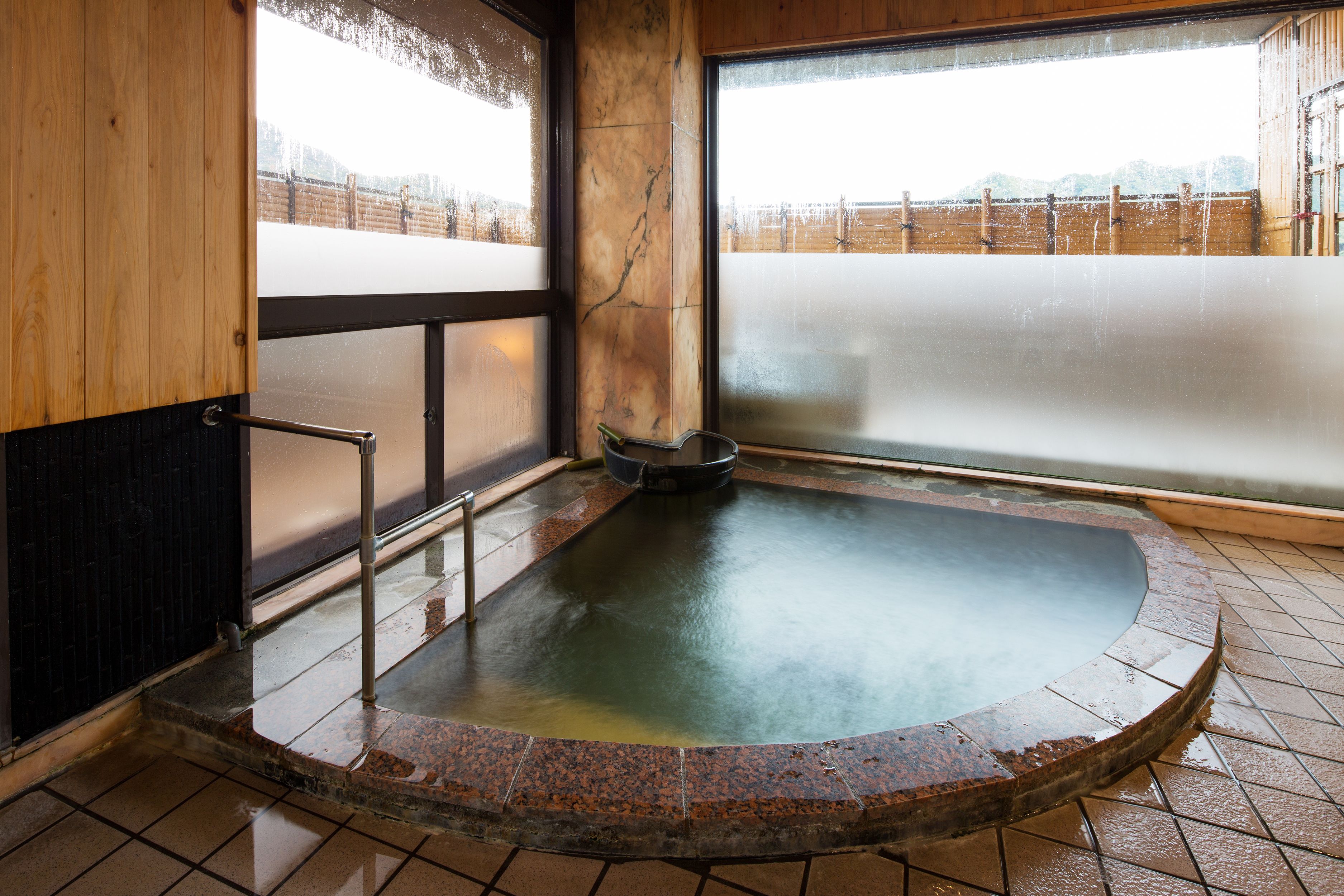 A hot spring bath with a wooden bench and a metal railing.