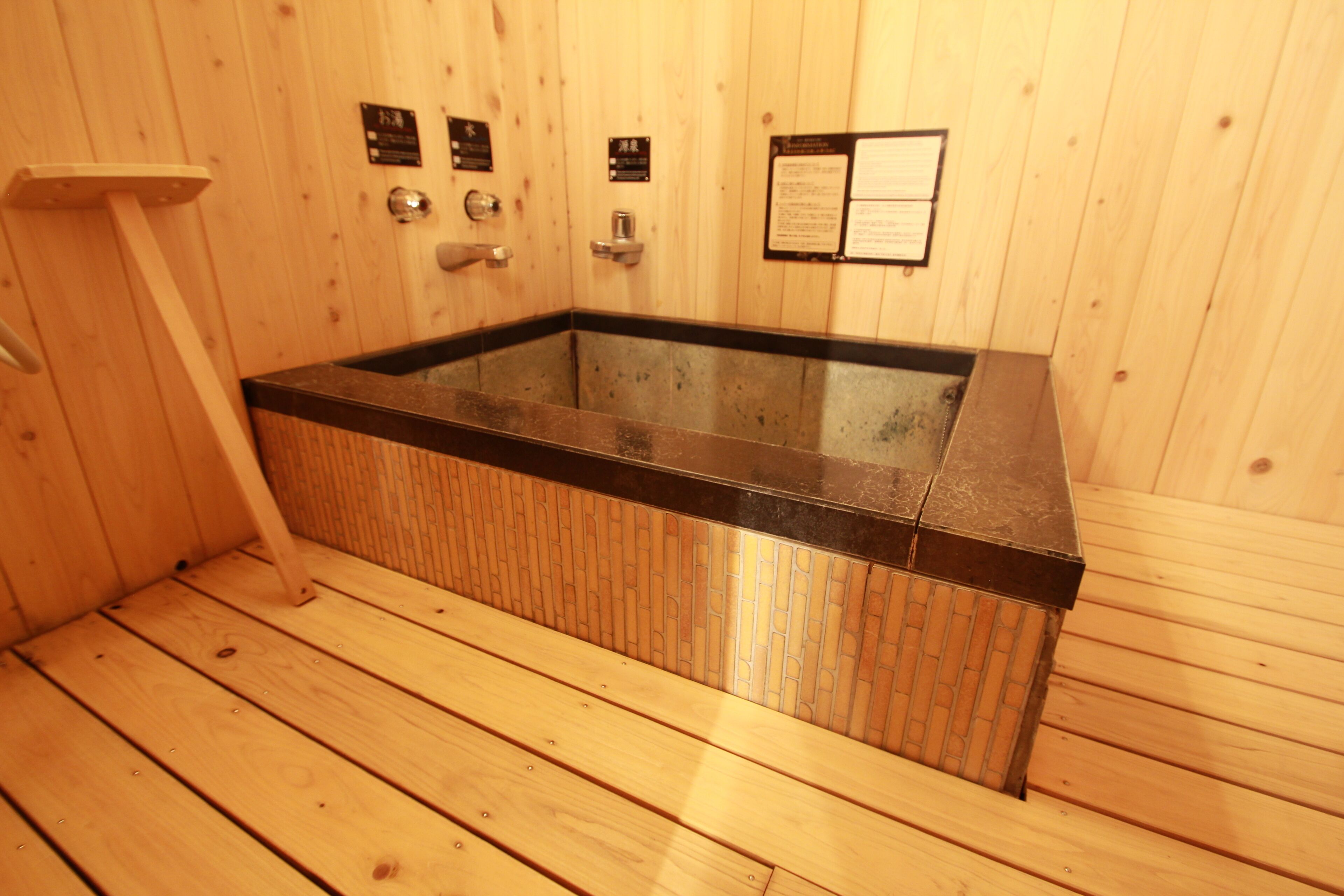 A wooden sauna with a glass-enclosed hot tub, wooden benches, and informational plaques on the walls.