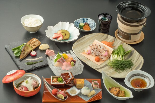Forskellige japanske retter anrettet på et bord, herunder ris, sashimi og syltede grøntsager.