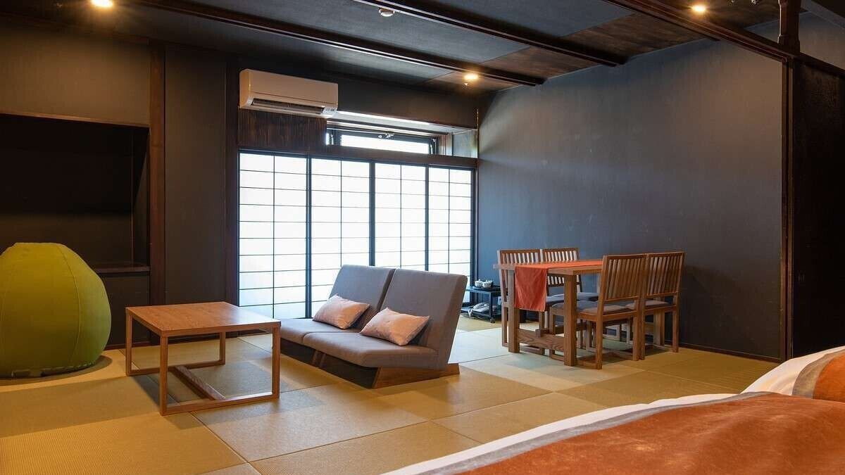 A room with a sofa, a small table, a dining table with chairs, and a large window.
