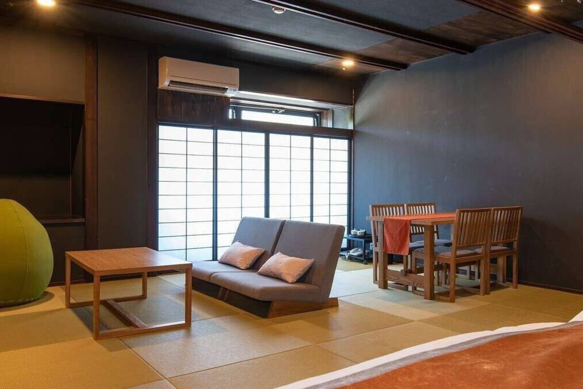 A room with a sofa, a small table, a dining table with chairs, and a large window.
