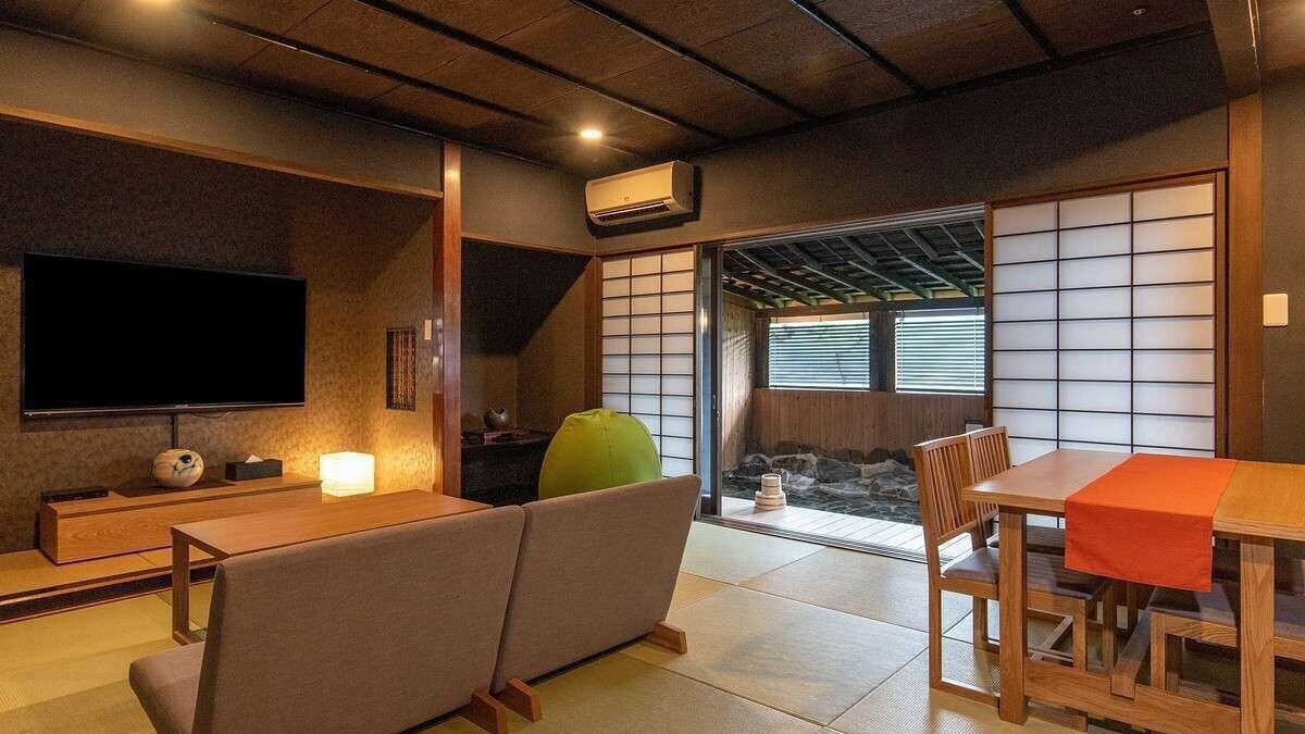 A traditional Japanese room with tatami flooring, a tatami mat sofa, a low wooden table, and a sliding door leading to a view of a waterfall.