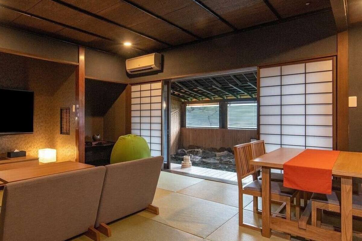 A traditional Japanese room with tatami flooring, a tatami mat sofa, a low wooden table, and a sliding door leading to a view of a waterfall.