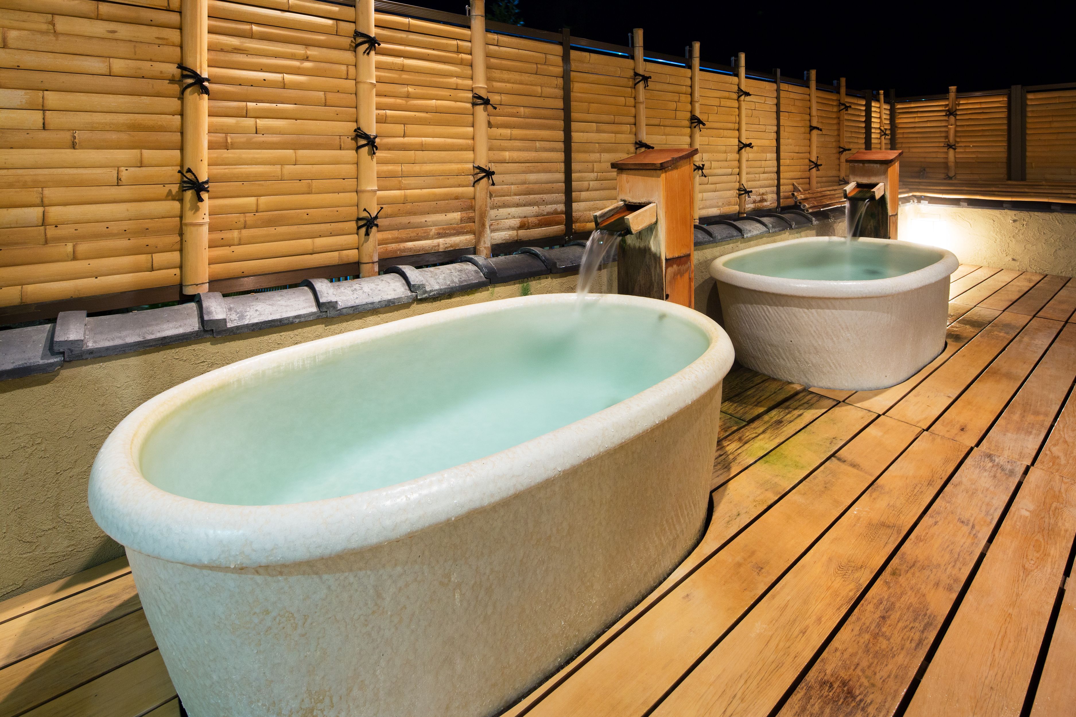 Een traditioneel Japans onsen met twee stenen hottubs en bamboe wanden.