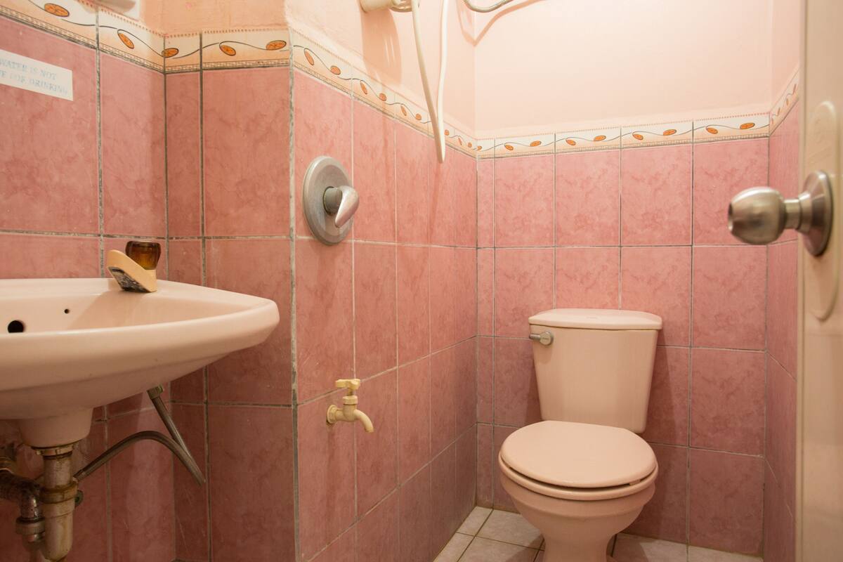 A bathroom with pink tiles, a white sink, a toilet, and a shower door.