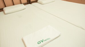 A clean, unmade bed with a folded white towel and a branded hotel towel. - GV Hotel Masbate (Masbate City)