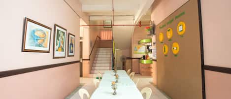 A hallway with a long table set for dining, framed artwork on the walls, and a sign indicating budget rooms.