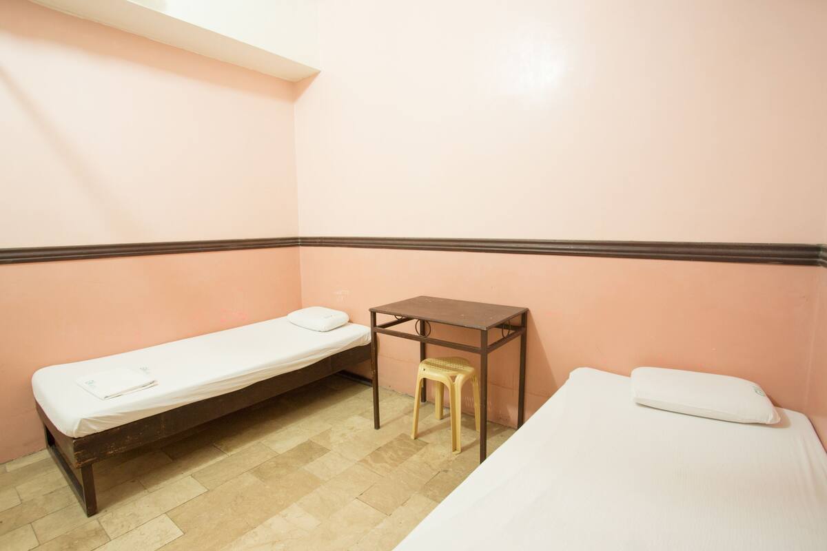 A small, single-bed room with a wooden table and a stool.