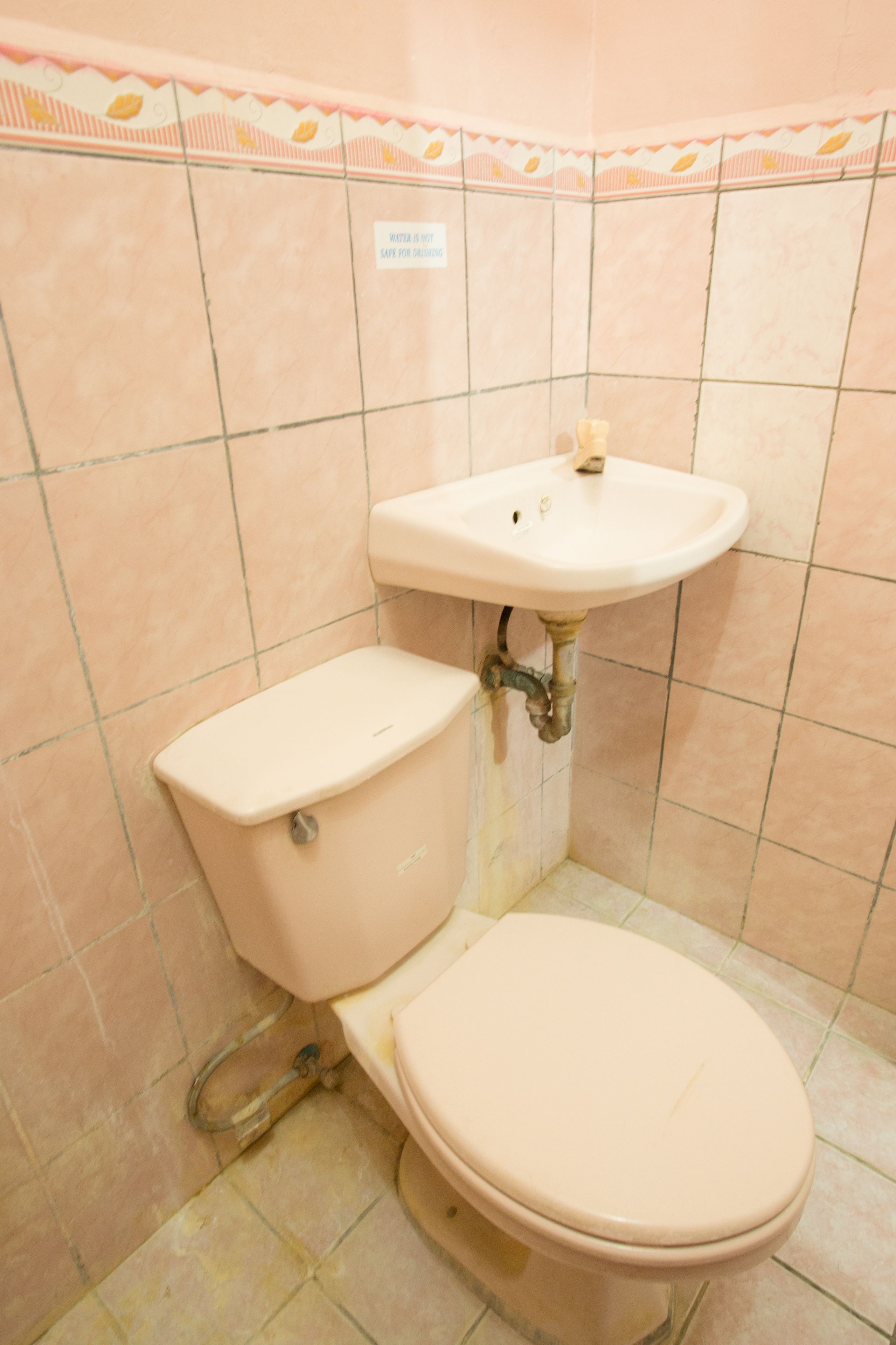 A bathroom with a toilet and sink, tiled walls, and a sign indicating water conservation.