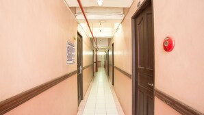 A long, narrow hallway with doors on both sides, a red fire alarm on the right wall, and a ceiling with visible pipes and a light fixture. - GV Hotel Masbate (Masbate City)