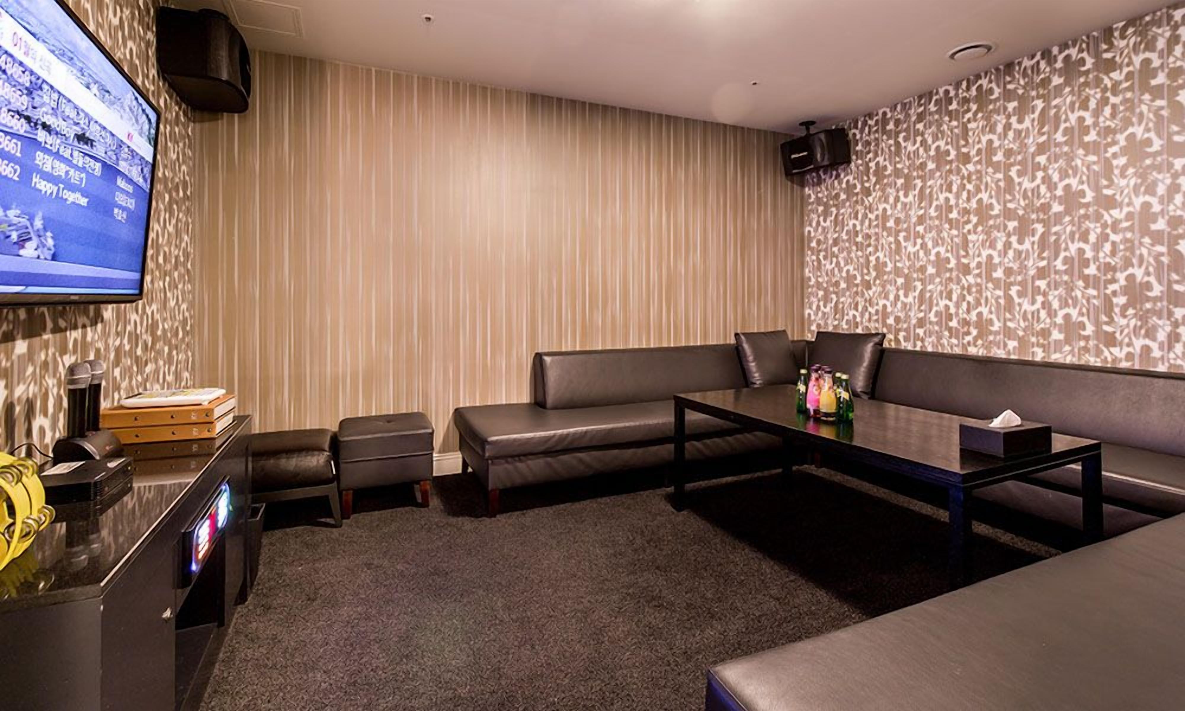 A modern living room with a flat-screen TV, leather sofas, a coffee table, and a carpeted floor.