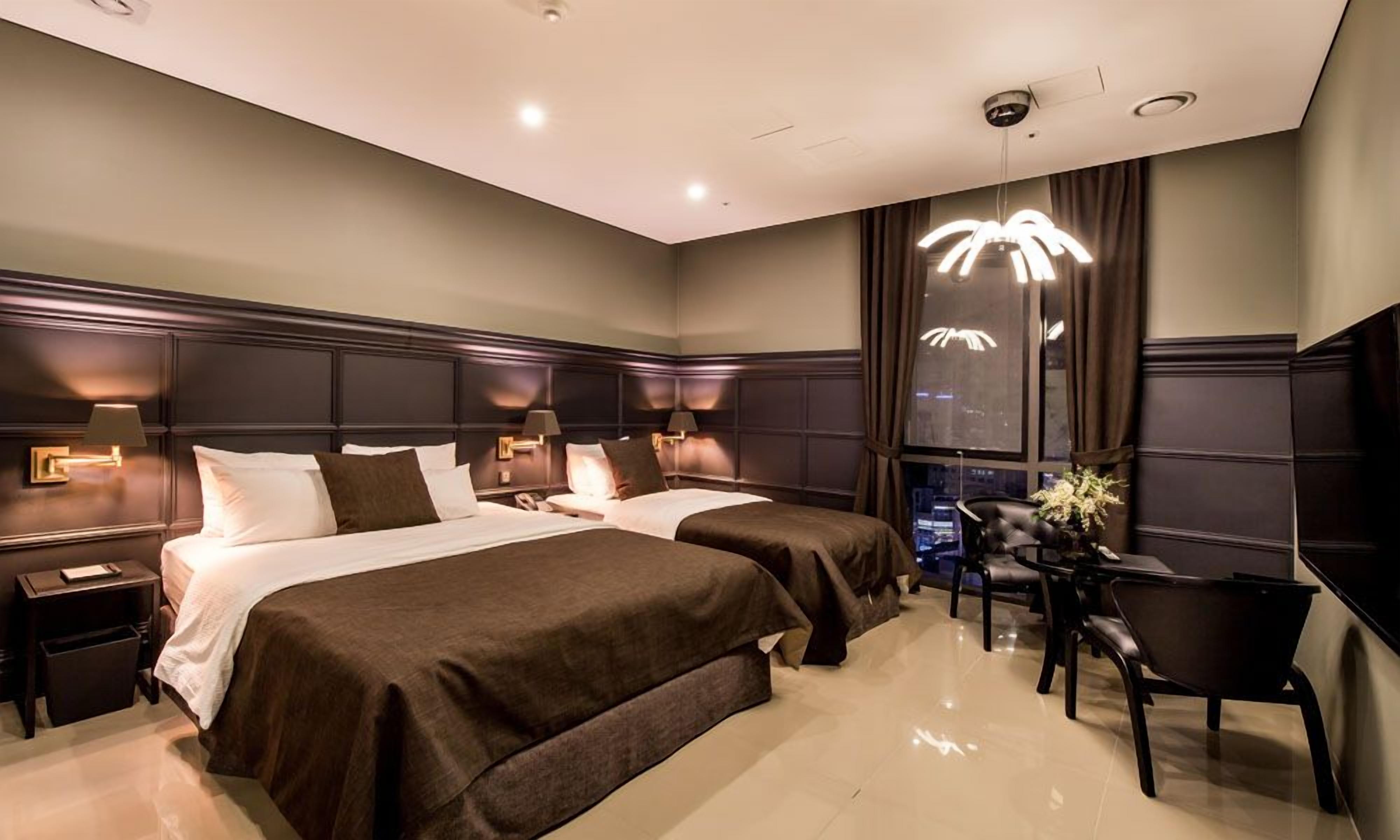 Une chambre d’hôtel avec deux lits, un coin salon avec une table et des chaises, et une grande fenêtre donnant sur un beau paysage.