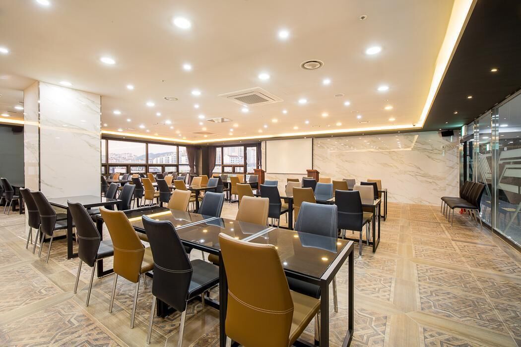 A conference room with multiple tables and chairs, large windows, and a city view.