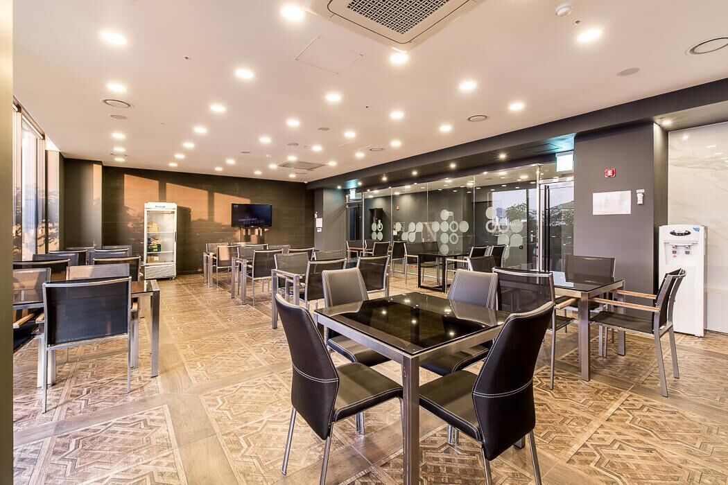 A modern conference room with glass tables and chairs, a large screen, and a refrigerator.